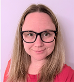 Portrait of a woman with shoulder-length blond hair, wearing black glasses and a pink top, smiling at the camera against a light pink background.